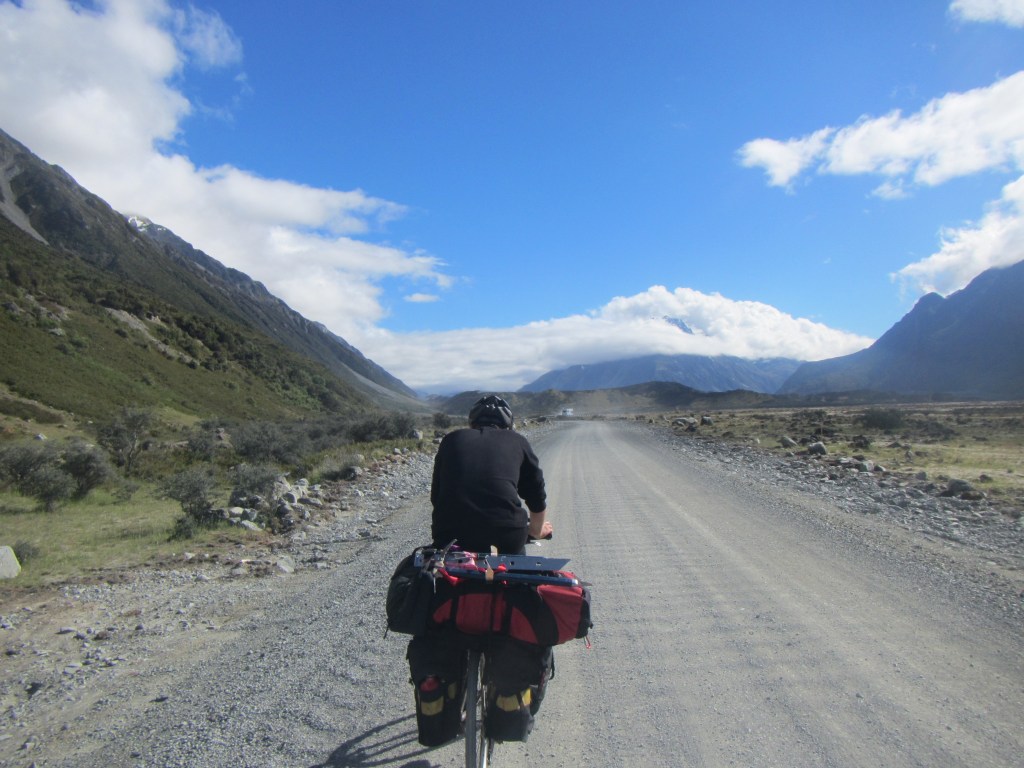 Alan Silva cycling up the Tasman Valley Road with his climbing pack strapped to  the back of his bike.