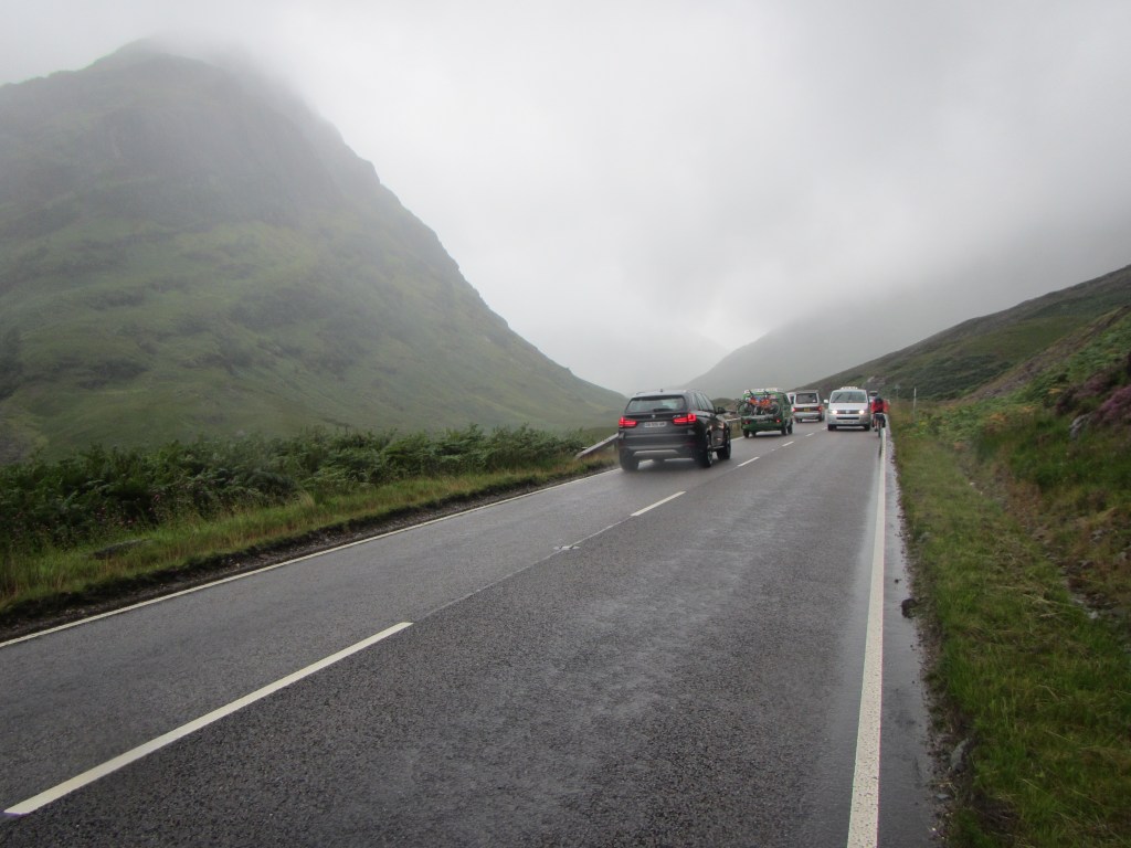 Alan cycles carefully along the non-existent road shoulder in heavy holiday traffic through the Glencoe valley
